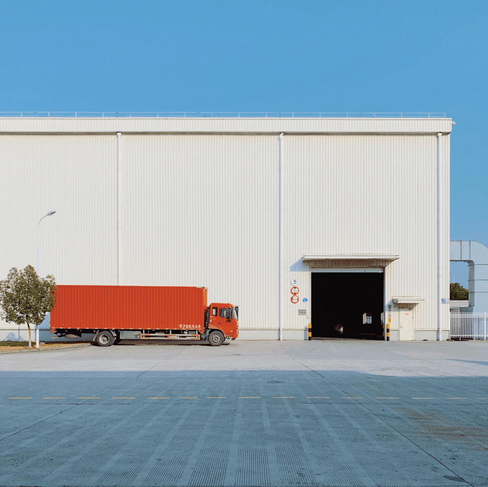 Orange Cargo Truck Parked In Front of Large White Warehouse