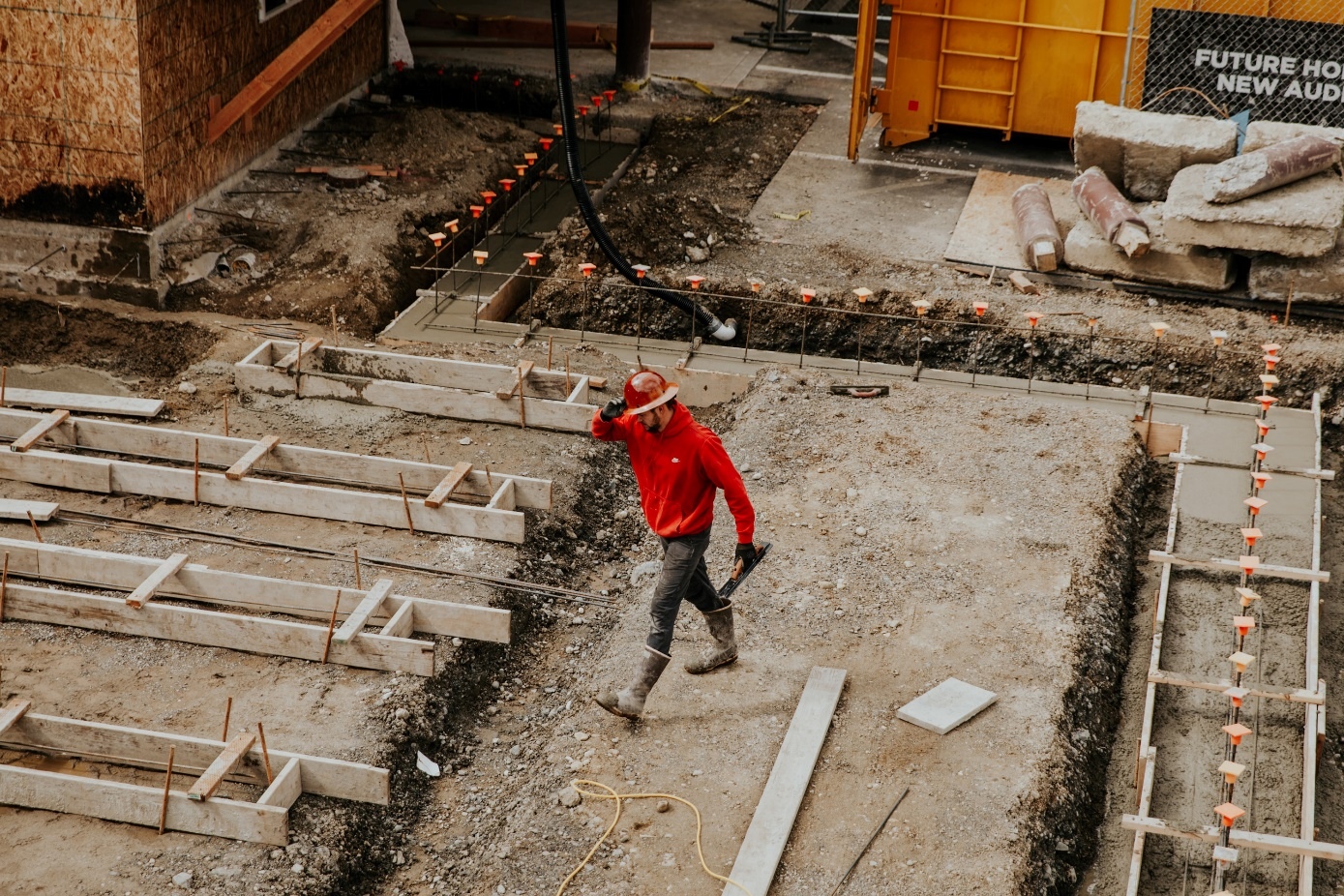 Construction Worker In Red Hoodie Walks Through Dirt Foundation of New Building