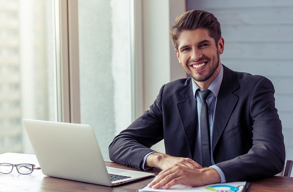 Businessman Sitting At Desk Smiling At Camera