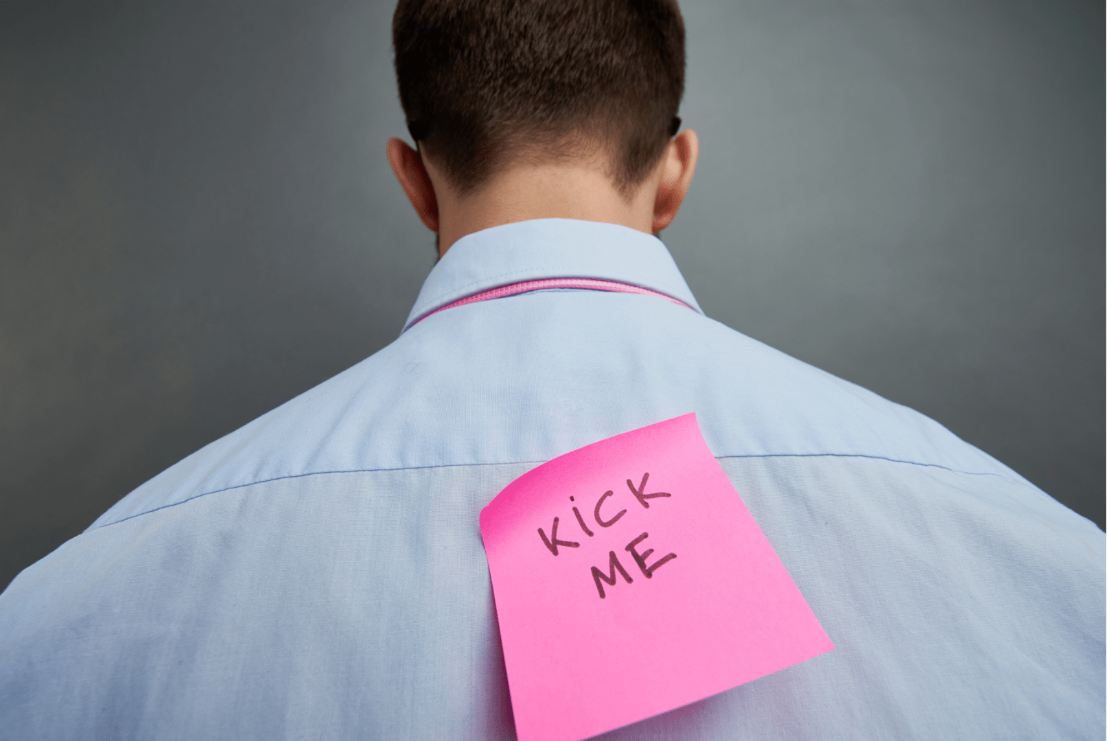 Male Employee With Pink Kick Me Sticky Note On Back