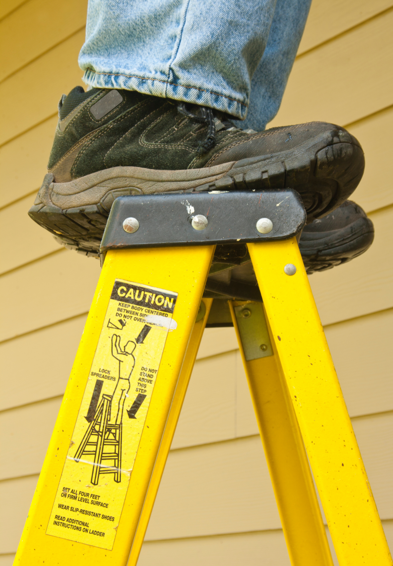 Man Standing On The Very Top Of A Yellow Ladder