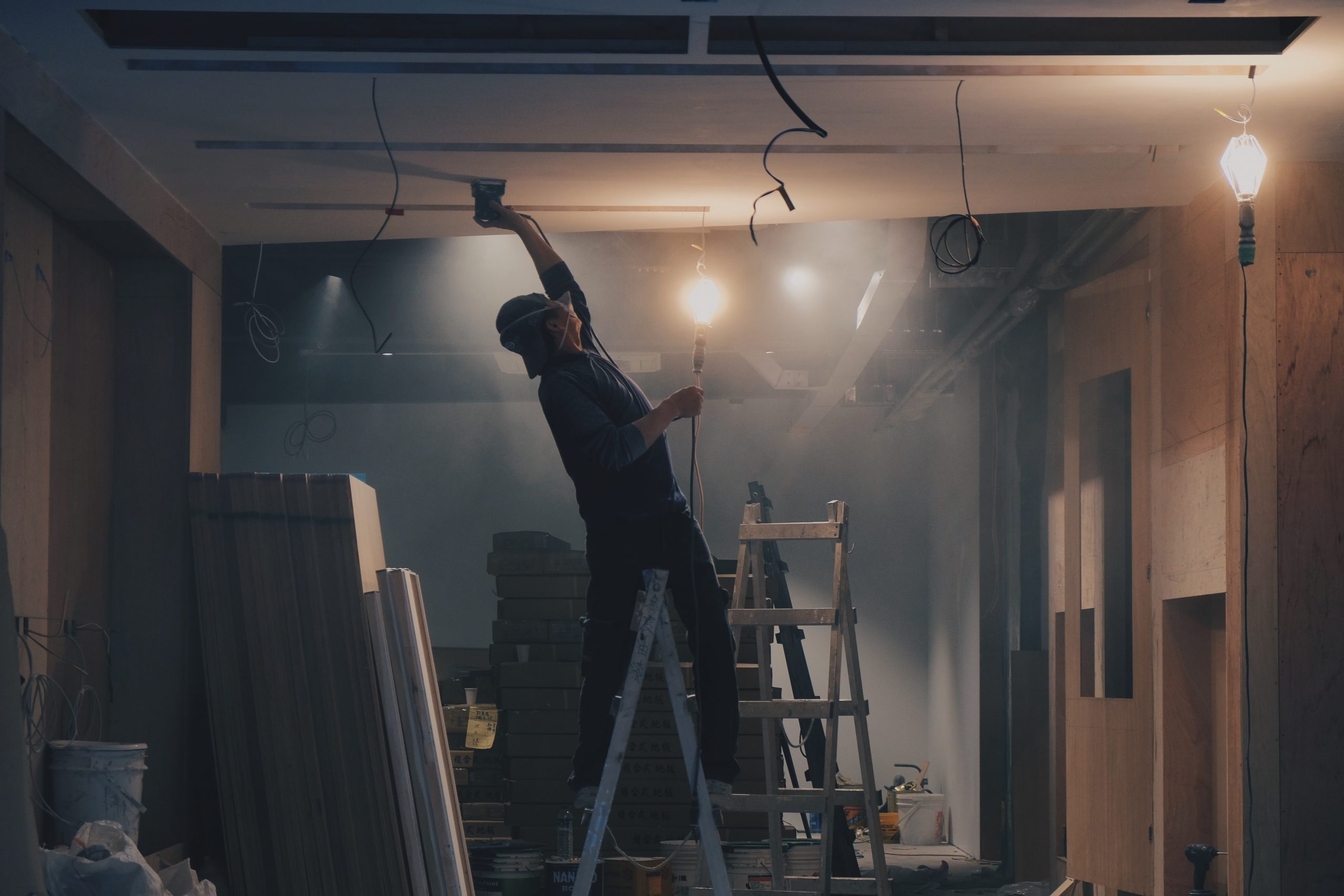 Man Straddling Ladder While Sanding Ceiling In Dark Dusty Room Man Straddling Ladder While Sanding Ceiling In Dark Dusty Room