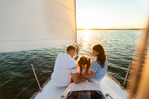 Family Yacht Sailing. Parents And Little Daughter Sitting Together On Sailboat Deck Hugging Enjoying Sea Trip. Back View, Free Space