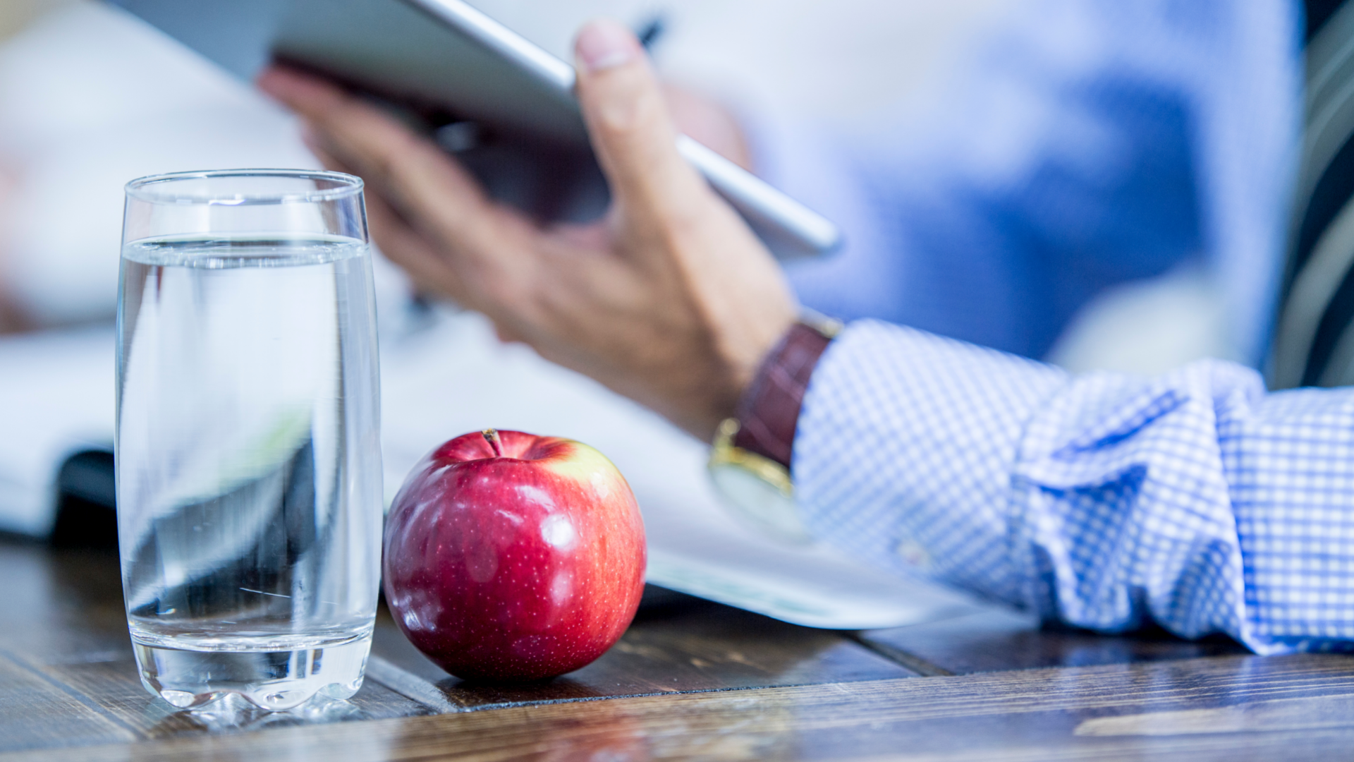 Red Apple and Glass of Water in Foreground with Businessman Working In Background