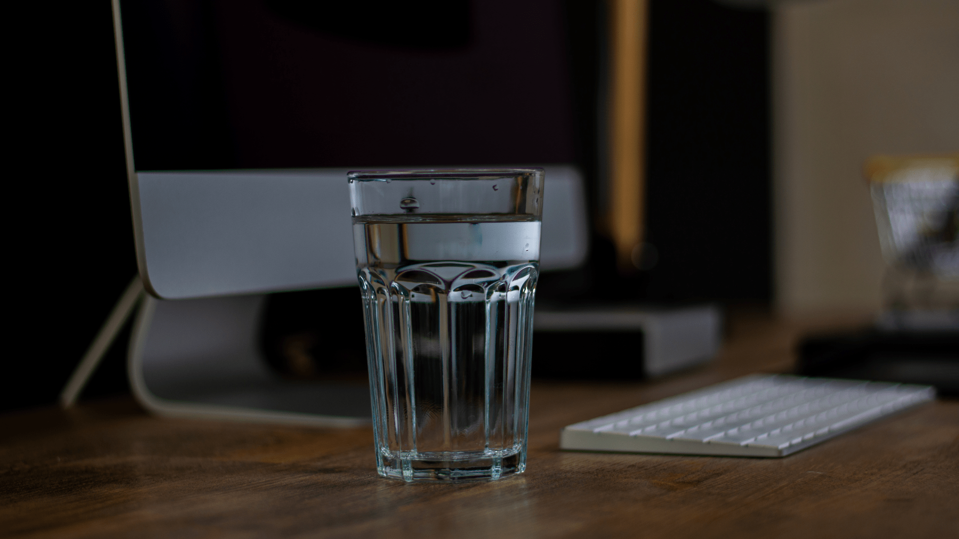 Glass of Water on Desk with Computer and Keyboard in Background