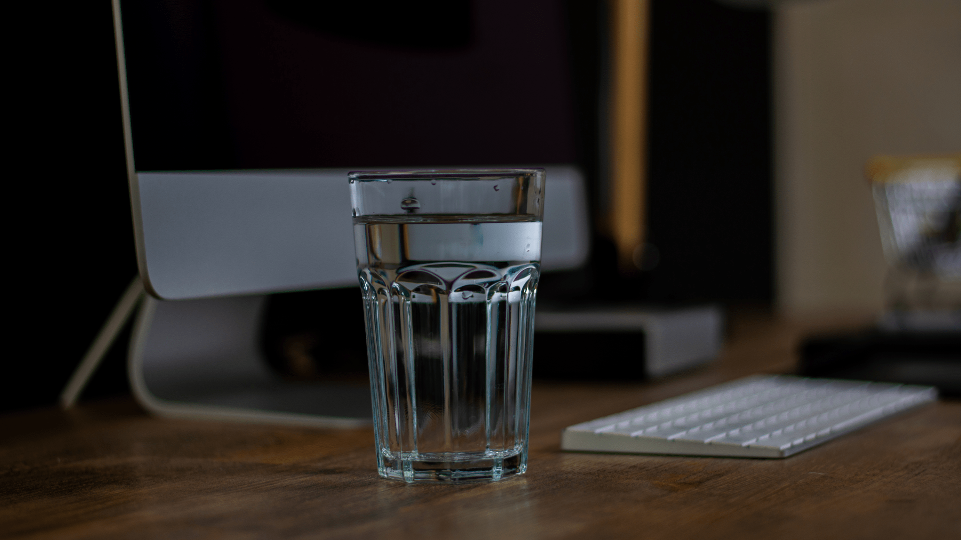 Glass of Water on Desk with Computer and Keyboard in Background Glass of Water on Desk with Computer and Keyboard in Background
