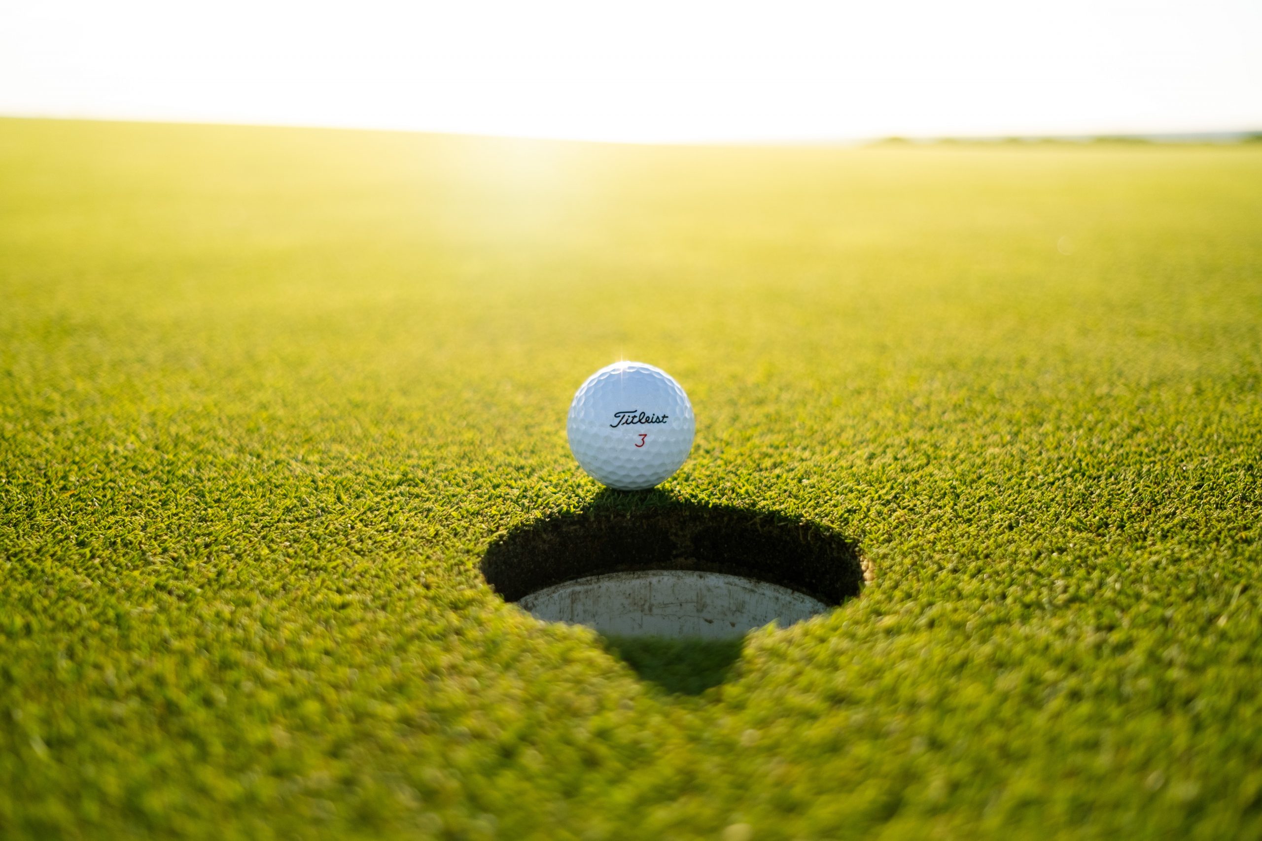 Golf Ball on Edge of Hole at Sunset Golf Ball on Edge of Hole at Sunset