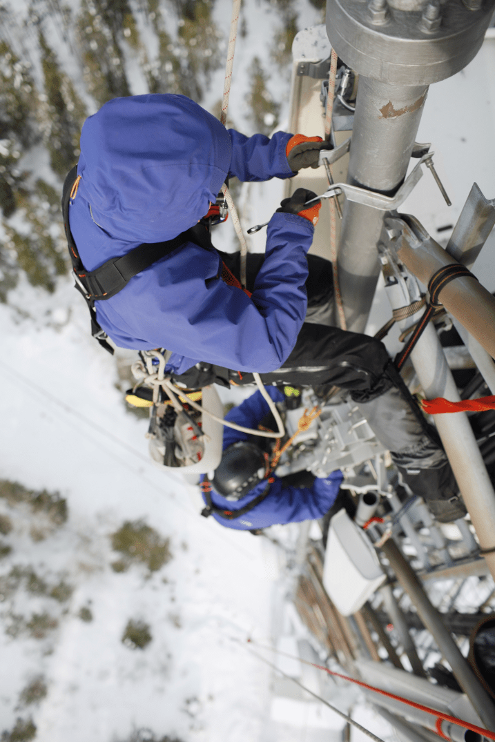 Two Telecommunication Workers Harnessed to Top of Tower in the Snow