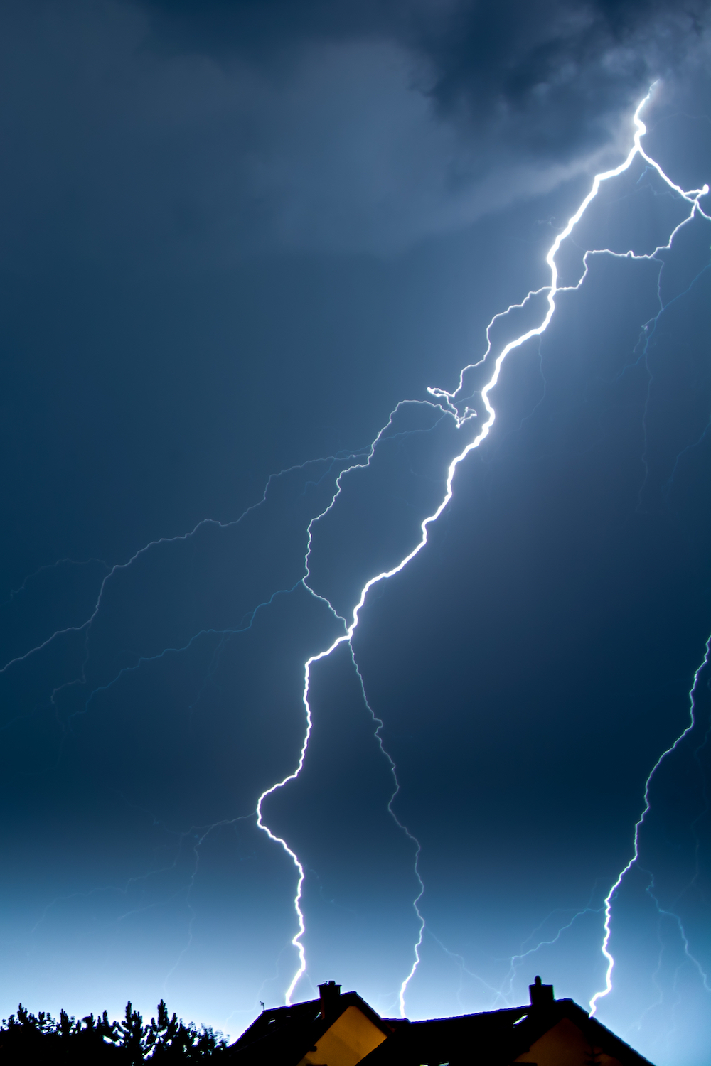 Vertical shot of lightning in the night sky over the village houses Tower Street Insurance Loss Control OSHA Safe and Sound Week Safety and Health